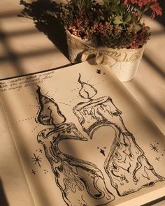 an open book sitting on top of a table next to a flower pot and plant