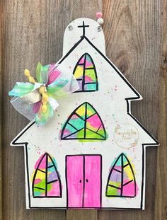 a paper house ornament hanging on a wooden wall with a ribbon and bow