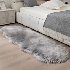 a bedroom with a white bed and gray fur rugs on the floor next to it