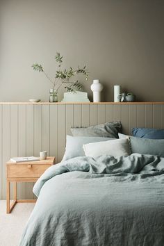 a bed with grey linens and white vases on the headboard above it