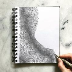 a person is holding a pen and drawing on a spiral notebook with an intricate design