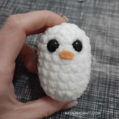 a hand holding a small white crocheted penguin