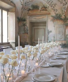 a long table is set with white flowers and candles for a formal dinner or party