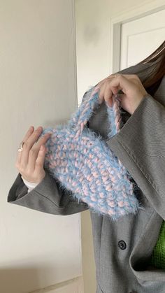 a woman wearing a gray coat holding up a blue and pink knitted mitt