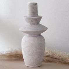 a white vase sitting on top of a wooden table next to a dry grass pile