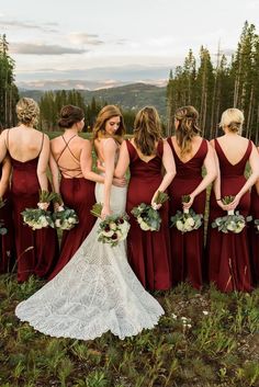 a group of bridesmaids standing in the grass with their dresses pulled back and holding bouquets