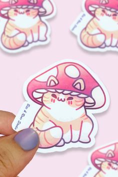 a hand holding up a pink sticker with an image of a cat and mushroom on it