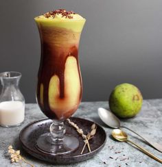 a glass filled with liquid next to two spoons and some fruit on a table