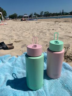 two insulated water bottles sitting on a towel at the beach