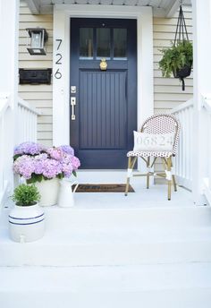 the front porch is decorated with purple flowers and potted plants on either side of the door