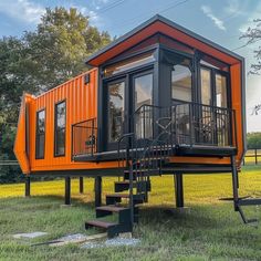 an orange and black tiny house in the middle of a field with stairs leading up to it