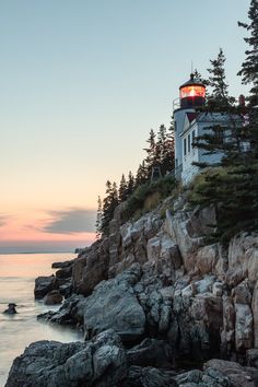 a light house sitting on top of a rocky cliff next to the ocean at sunset