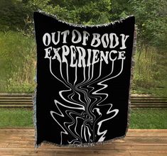 a blanket with the words out of body experience printed on it in front of some trees