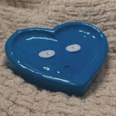 a blue heart shaped object laying on top of a bed with eyes drawn on it