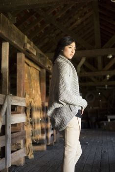 a woman standing in front of a wooden door wearing a gray sweater and white pants