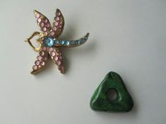 two brooches are sitting on a table next to each other, one has a green triangle and the other is a pink flower