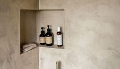 two bottles are sitting in a niche on the wall next to a towel and soap dispenser