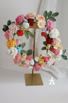 a crocheted wreath on a stand with flowers in the middle and leaves around it