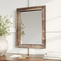 a mirror sitting on top of a wooden table next to a vase filled with flowers