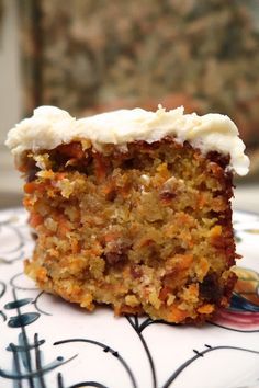 a piece of carrot cake with white frosting on a decorative plate, sitting on a table