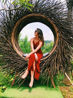 a woman in a red dress is sitting on a large circular object made out of branches