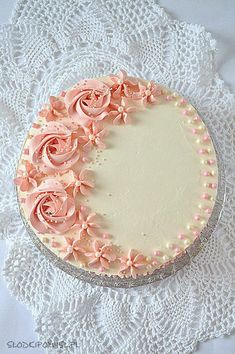 a cake with pink frosting and roses on it sitting on a lace doily