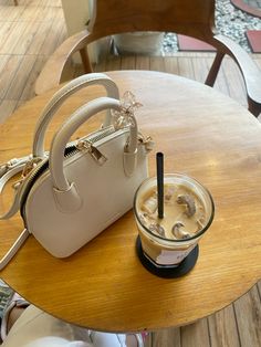 a white purse sitting on top of a wooden table next to a small cup filled with liquid