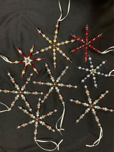 four beaded snowflakes are arranged on a black background with white and red ribbons