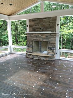 an empty porch with wood flooring and a stone fireplace in the center surrounded by trees