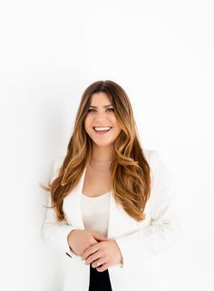 a smiling woman in a white blazer and black pants standing with her arms crossed