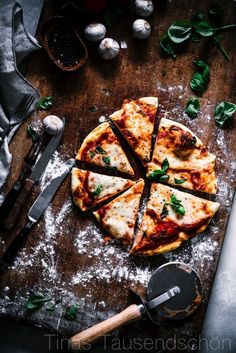 a sliced pizza sitting on top of a wooden cutting board next to garlic and pepper