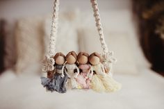 three little dolls hanging from a rope on a bed with white sheets and pillows in the background