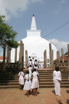 several women in white dresses are walking up some steps to a large structure with columns