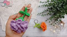 someone is holding a crocheted flower keychain in front of some flowers