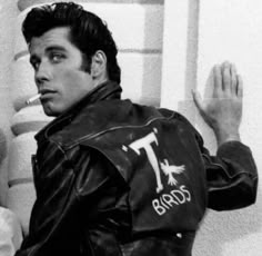 a black and white photo of a man in a leather jacket leaning against a wall