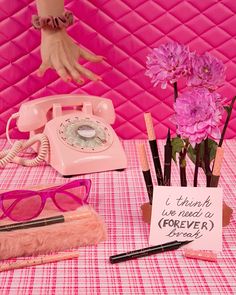 a table topped with pink flowers and eyeglasses next to an old fashioned phone