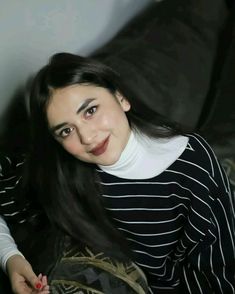 a woman sitting on top of a couch next to a black and white striped shirt