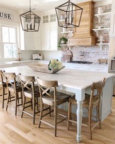 a kitchen with white cabinets and wooden chairs in front of an island table surrounded by hanging lights