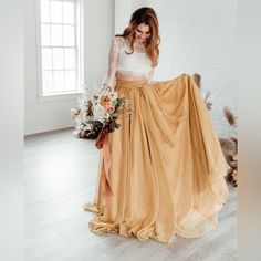 a woman standing in a room with a long skirt and flowers on her head, holding a bouquet