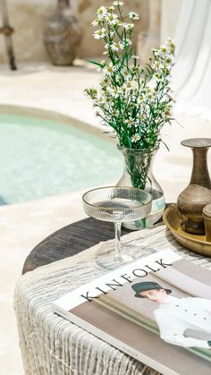 vases with flowers on a table next to a swimming pool and magazine holder in the foreground