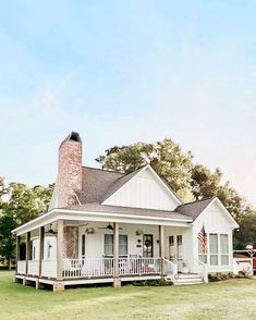 a white house sitting on top of a lush green field next to a tall brick chimney