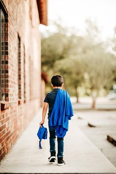 a young man walking down a sidewalk with a blue blanket on his back and an umbrella over his shoulder