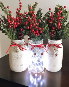 three mason jars with red berries and greenery are sitting on a table next to each other