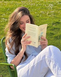 a woman sitting in a green chair reading a book on the grass with daisies around her