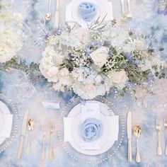 the table is set with white and blue flowers, silverware, and napkins