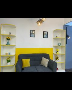 a grey couch sitting in front of a yellow and white book shelf filled with vases