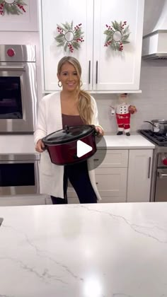 a woman standing in a kitchen holding an open crock pot