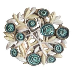 a white and blue brooch with leaves on it's center, in the shape of a circle