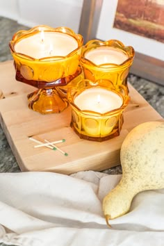 three candles sitting on top of a wooden cutting board next to a pear and some other items