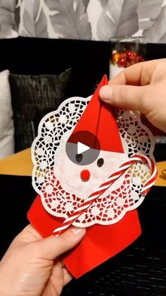 someone is holding up a red and white origami santa clause decoration on a table